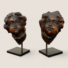 Load image into Gallery viewer, Ziebarth's Antiques pair of hand-carved wooden cherub head sculptures on minimalist black metal stands.